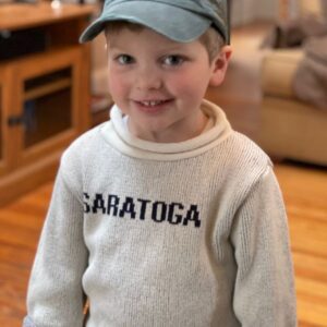 Natural color Cotton/Polyester blend sweater with Saratoga in Navy across chest. Rolled neck, sleeve and hem. Youth sizes displayed on model.