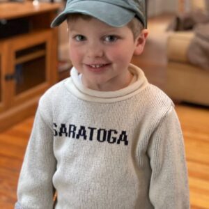 Natural color Cotton/Polyester blend sweater with Saratoga in Navy across chest. Rolled neck, sleeve and hem. Youth sizes displayed on model.